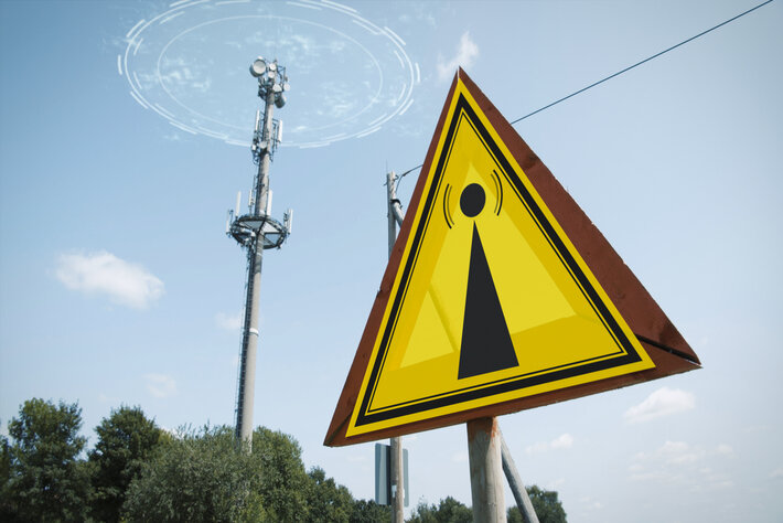 The EMF Warning Sign and a 5G tower causing radiation under a blue sky